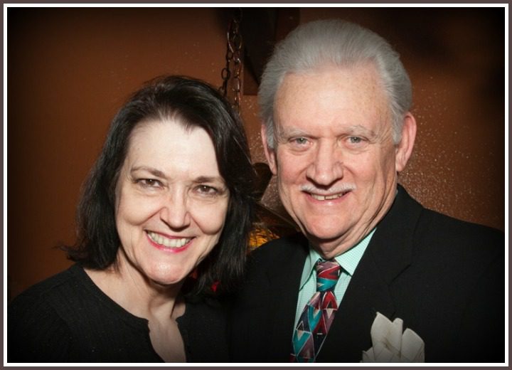 A Man and a Woman Standing Closely Together, the Man Is Wearing a Black Suit With a Patterned Tie and a White Pocket Square.